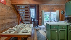A wooden cabin interior with a dining table set for four, a wood-burning stove, and a green kitchen area. - Powder Monkey 4: 2 Bedrooms Plus Sleeping Loft, 2 Full Baths: Slope Side (Snowshoe)