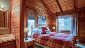A wooden cabin bedroom with a plaid bedspread, a nightstand with a lamp, and a window with curtains. - Powder Monkey 4: 2 Bedrooms Plus Sleeping Loft, 2 Full Baths: Slope Side (Snowshoe)
