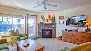 Una sala de estar con chimenea, ventilador de techo, televisor y vistas al exterior.
