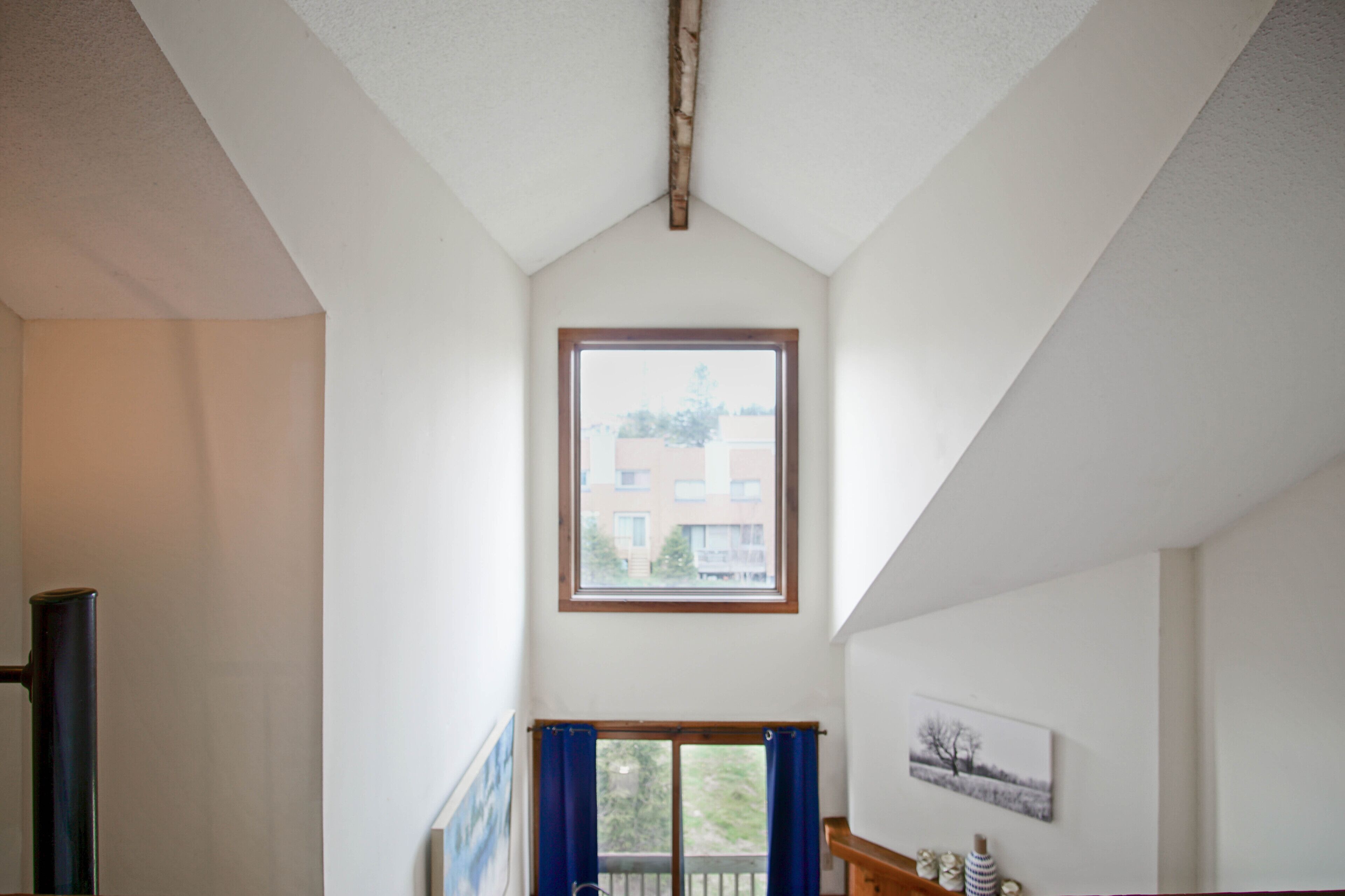 A high-ceilinged room with a large window, a door, and a picture on the wall.