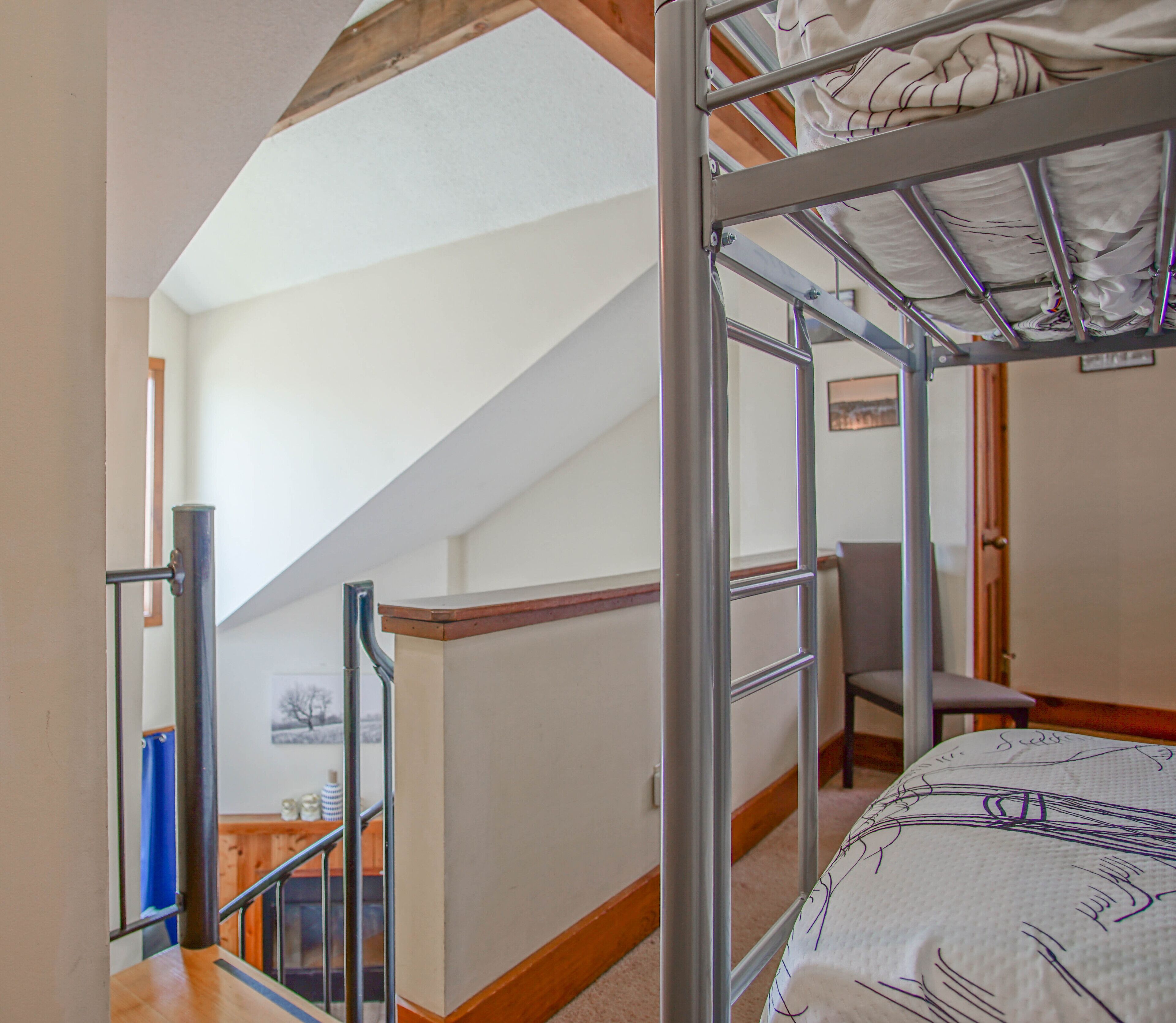 Ein Schlafsaalzimmer mit Etagenbett, Schreibtisch und Stuhl. Eine Treppe führt zu einer erhöhten Ebene.