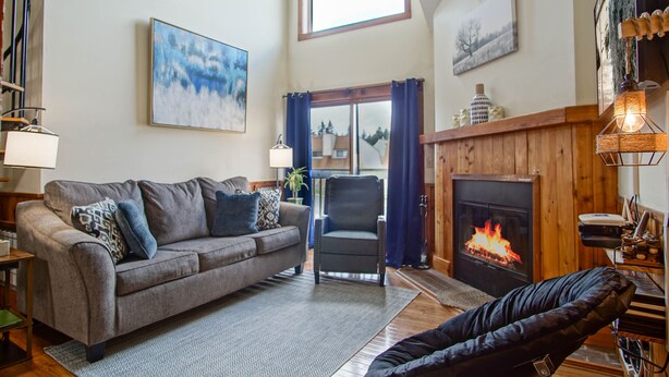 Una sala de estar acogedora con chimenea, un sofá, una silla y un rincón de lectura con lámpara.