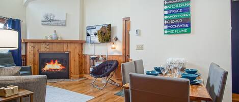 Een gezellige woonkamer met een open haard, een eethoek met blauw servies en een bord met daarop verschillende merken.