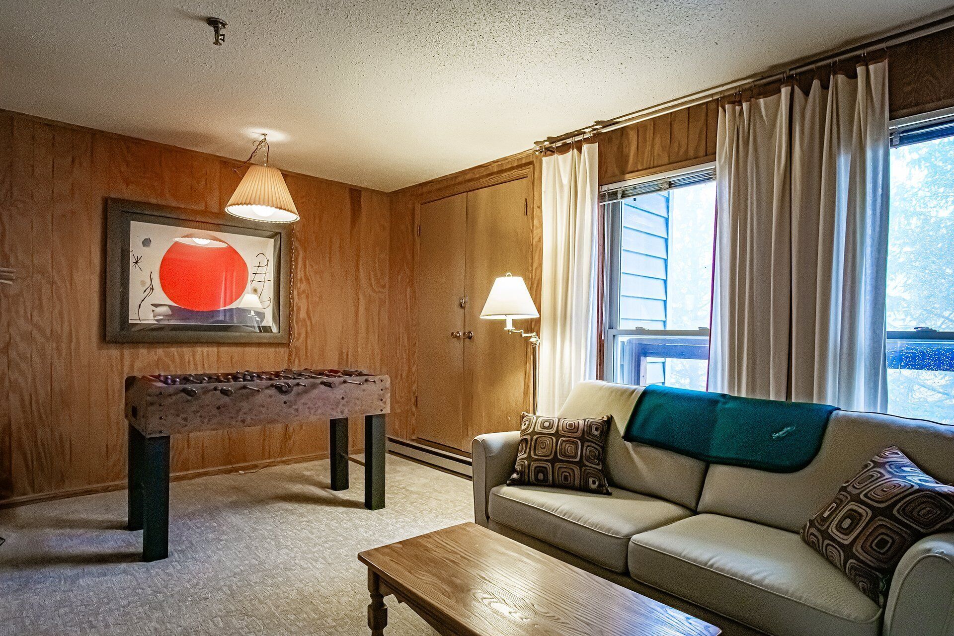 A cozy living room with a sofa, coffee table, and foosball table.