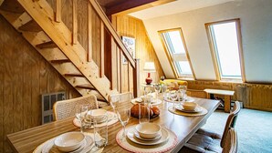 A dining area with a wooden staircase, a long table set for a meal, and large windows allowing natural light. - Leatherbark - 301b, 2 Bedroom Allegheny Sunrise Spacious Condo Foosball (Snowshoe)