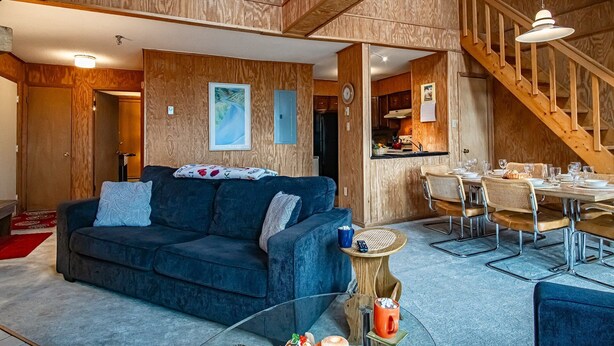 A cozy living room with a dark blue sofa, a glass coffee table, and a dining area with a wooden table and chairs. - Leatherbark - 301b, 2 Bedroom Allegheny Sunrise Spacious Condo Foosball (Snowshoe)