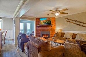 A cozy living room with a fireplace, comfortable seating, and a television mounted on a wooden wall. - Summit 107b 3Br Condo (Snowshoe)