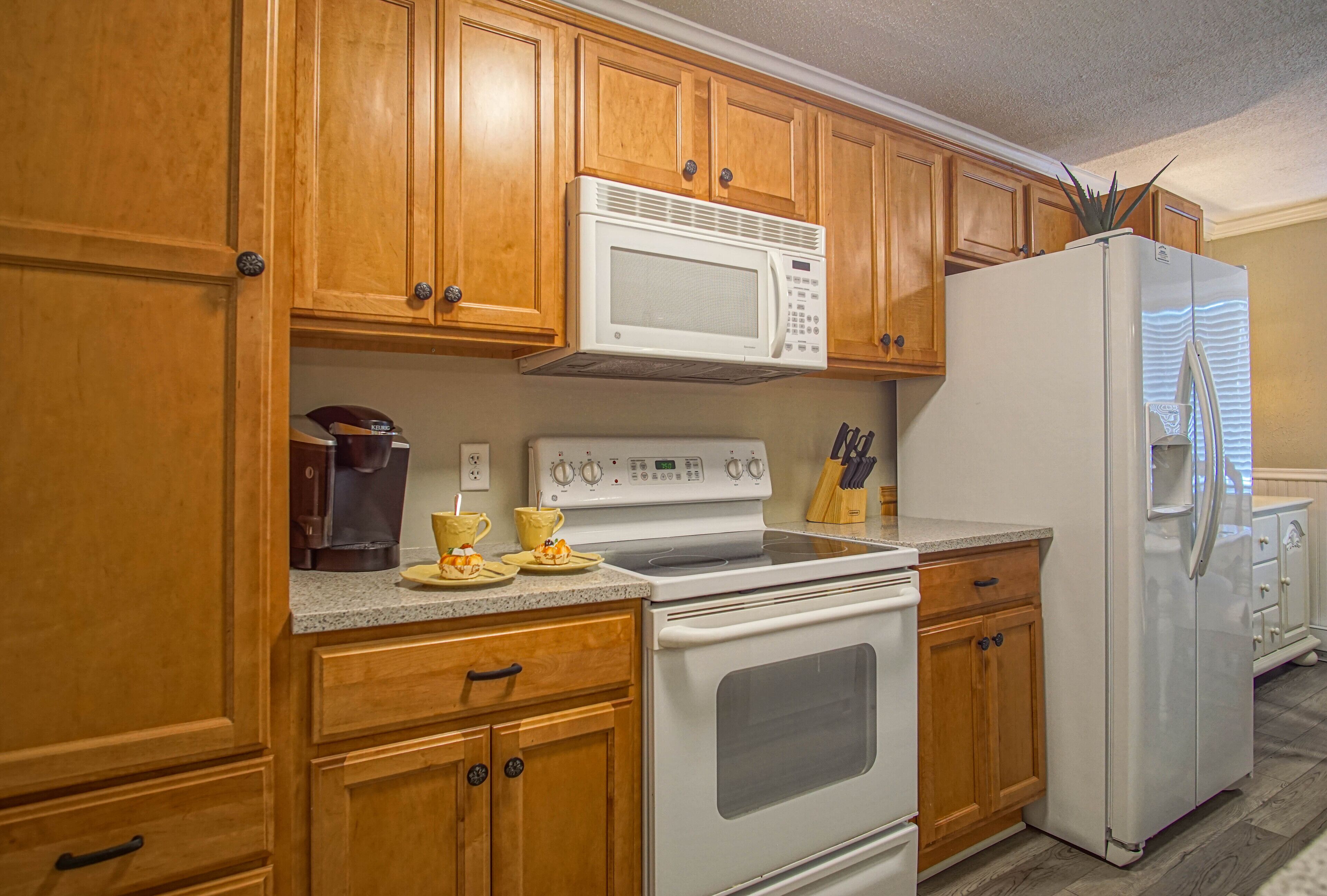 A kitchen with wooden cabinets, a white microwave, a stove, and a refrigerator.