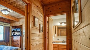 Een houten interieur met een bed, een televisie, een badkamer met houten kasten en een spiegel.