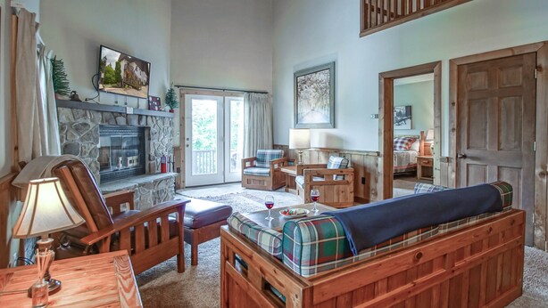 Een gezellige woonkamer met een stenen openhaard, houten meubels en een groot raam met gordijnen.
