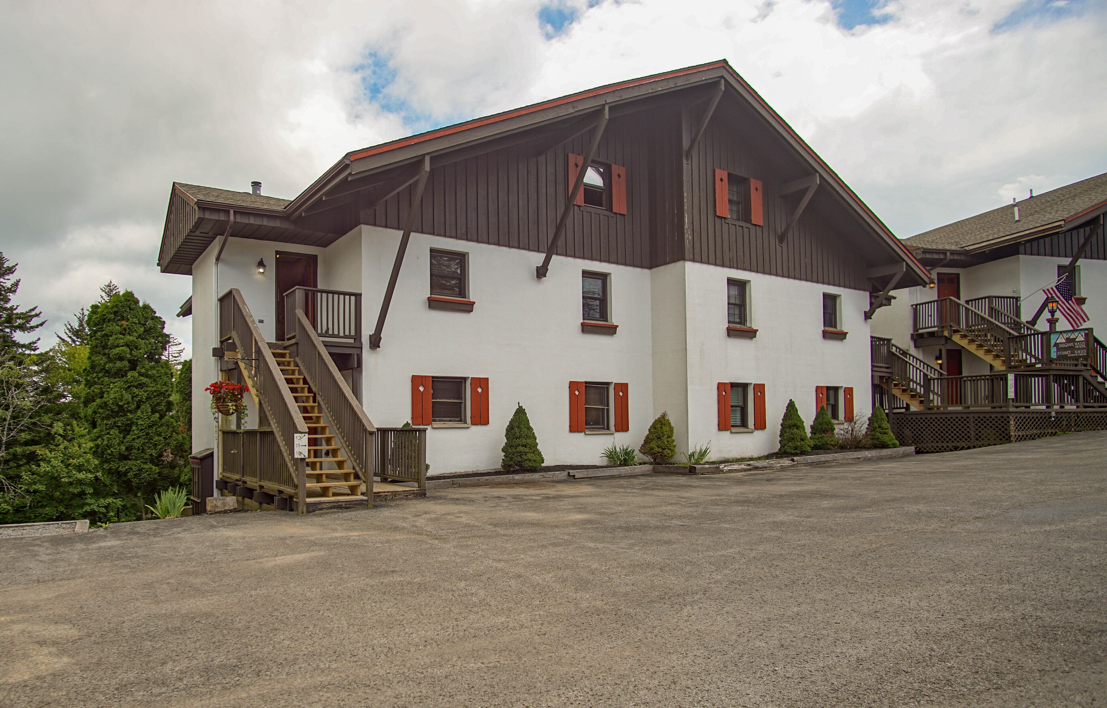 A two-story building with a wooden staircase leading to the entrance, a covered outdoor area, and a flag on the roof.