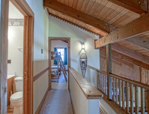 Uma escada de madeira com corrimão, que leva a um quarto com janela e luminária na parede.