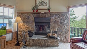 A stone fireplace with a framed picture above, a television on a wooden cabinet, and a lamp to the left. - Whistlepunk #24: 4 Bedroom, 3 Bath: Slope Side, Wood Fireplace (Snowshoe)