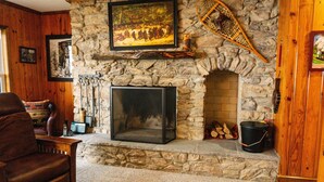 A stone fireplace with a framed picture above it, a wooden chair, and a stone wall. - Stemwinder #8:3 Bedroom/3.5 Bath Slopeside (Snowshoe)