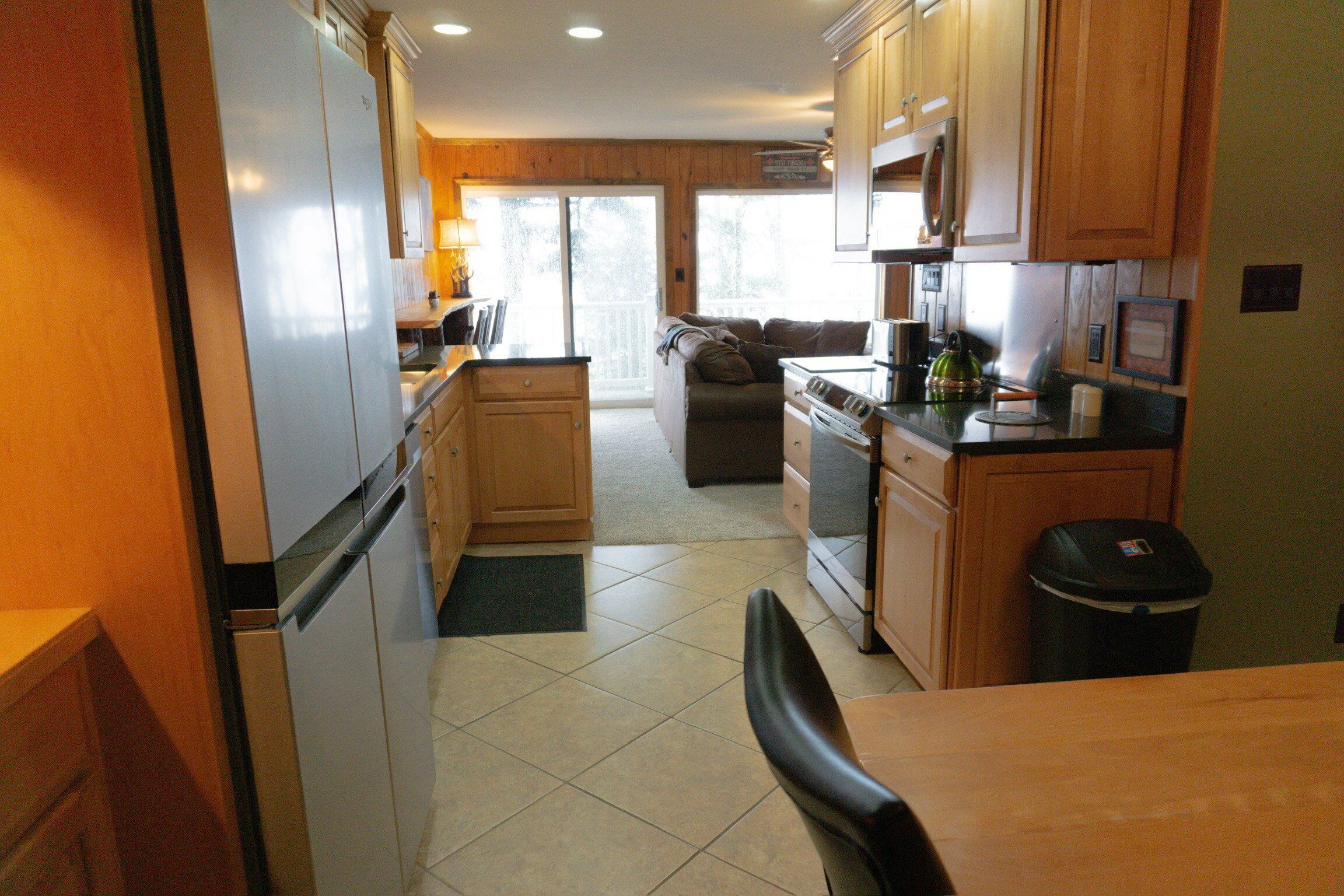A kitchen with wooden cabinets, a refrigerator, stove, and a dining area with a chair.
