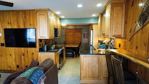A kitchen with wooden cabinets, a microwave, a dining area with a table and chairs, and a TV mounted on the wall. - Stemwinder #8:3 Bedroom/3.5 Bath Slopeside (Snowshoe)