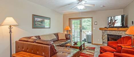 A living room with a brown leather sofa, a wooden coffee table, a red armchair, a fireplace, and a ceiling fan.