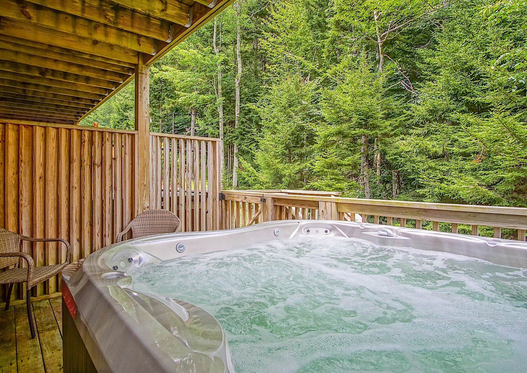 A hot tub on a wooden deck with a view of a forest.