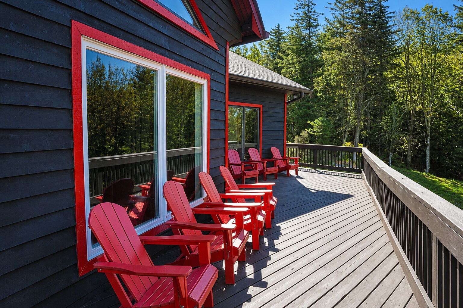 A wooden deck with red chairs and tables, overlooking a forested area.