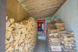 Un couloir étroit, bordé de piles de bois de chauffage de chaque côté, qui mène à une porte rouge.