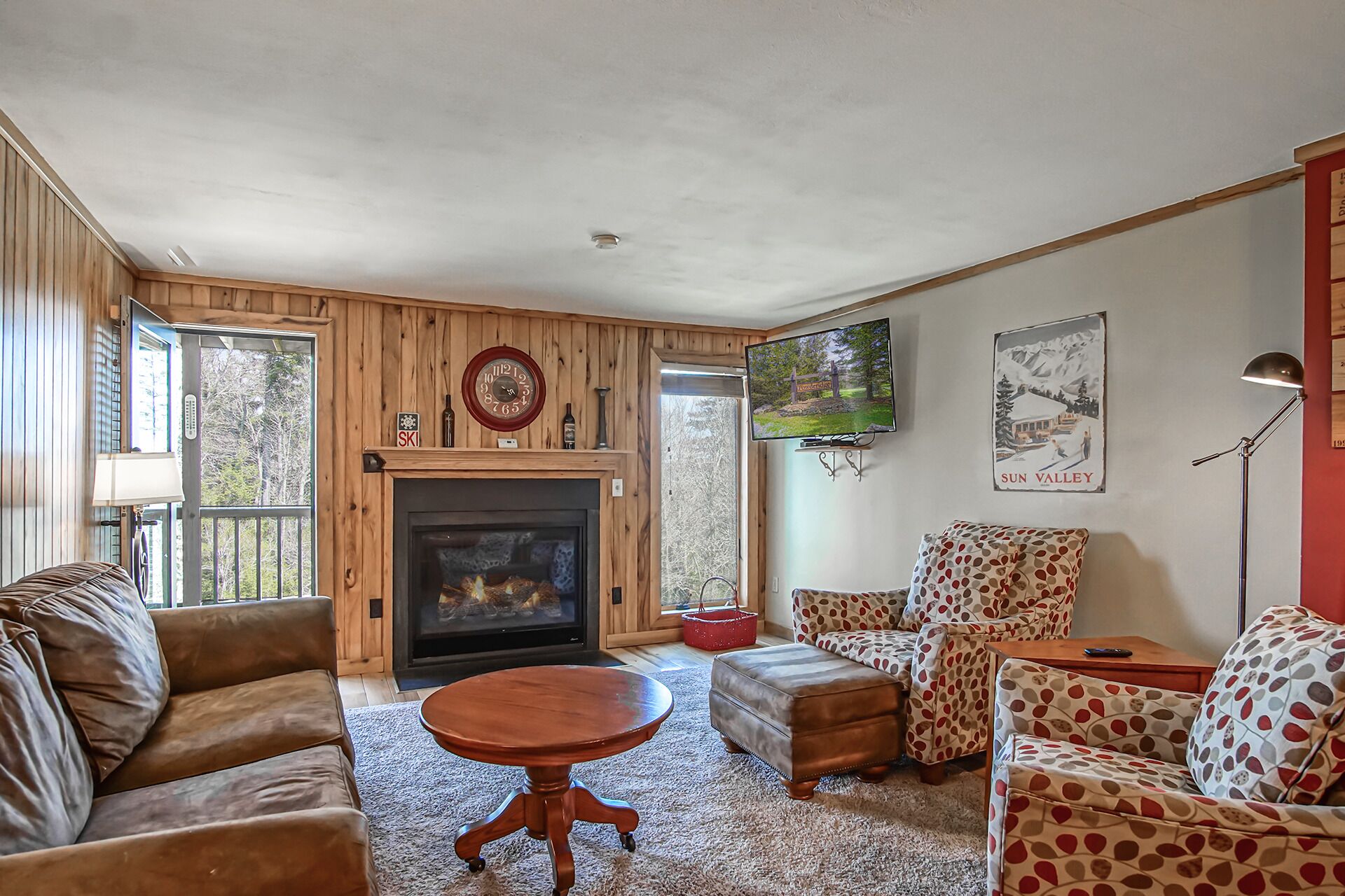 A cozy living room with a fireplace, wooden walls, and patterned furniture.