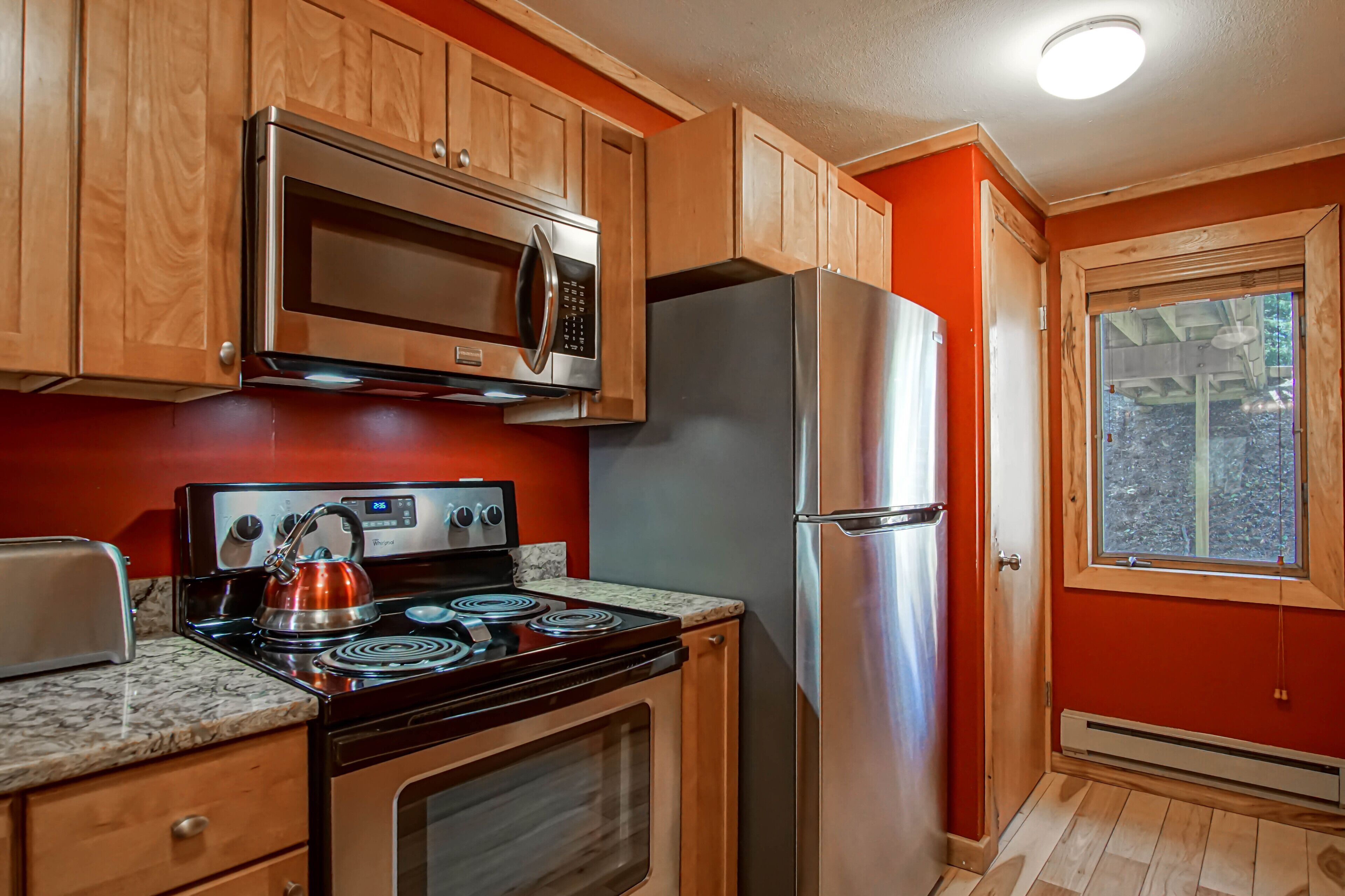 A kitchen with wooden cabinets, a stainless steel refrigerator, a microwave, a stove, and a toaster.
