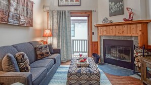 Una sala de estar acogedora con un sofá azul, cojines estampados, una chimenea de madera y vistas al exterior.