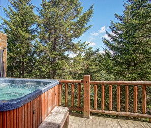 Une terrasse en bois avec un jacuzzi, entourée de grands arbres et sous un ciel dégagé.