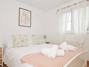 Une chambre à coucher avec un lit, des oreillers, une table de chevet, une lampe et une fenêtre avec des rideaux.