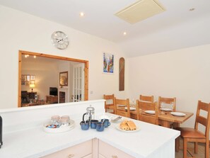 A dining area with a wooden table set for four, a coffee maker, and a clock on the wall. - Cribba (Port Isaac)