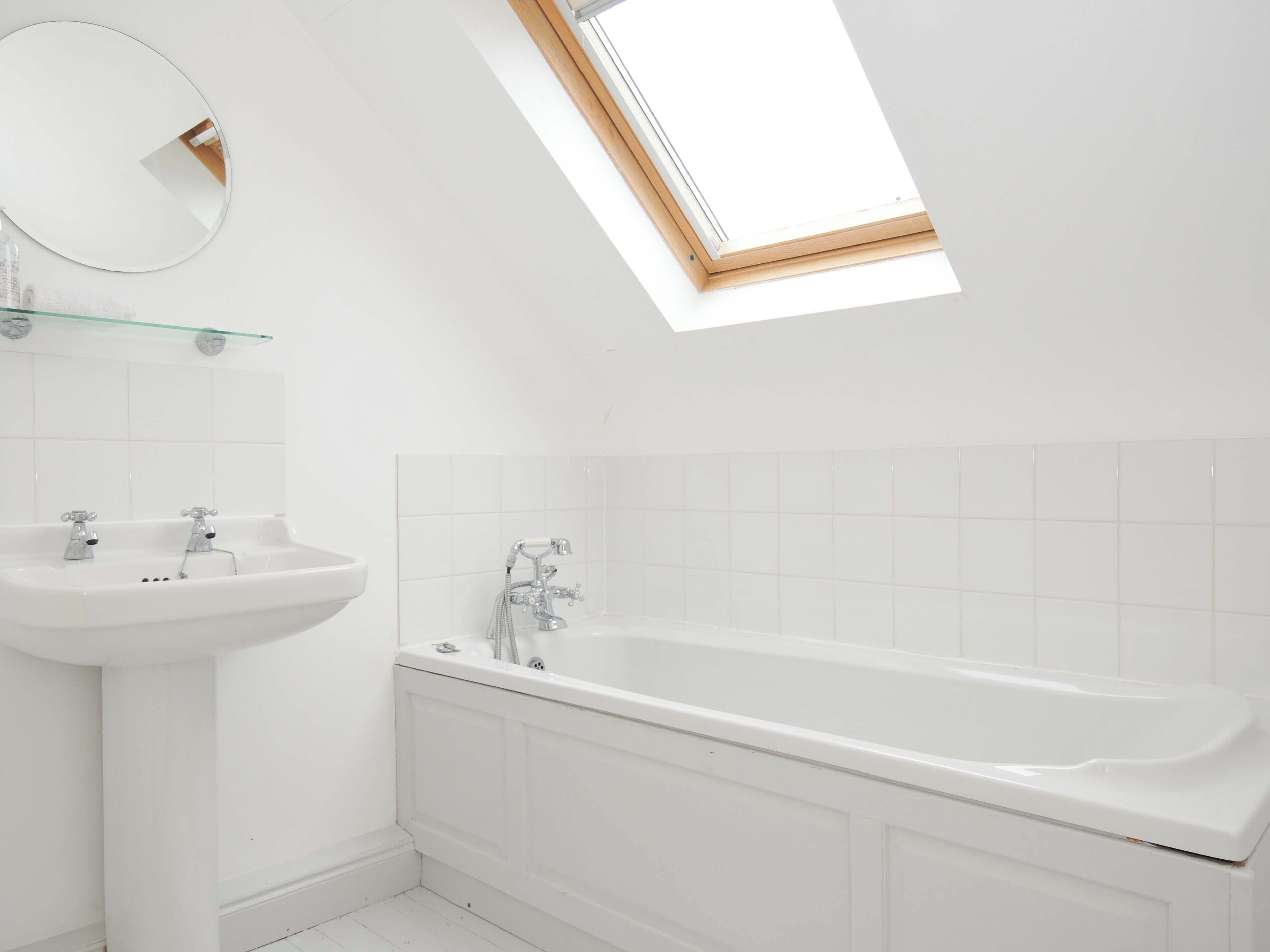 A modern bathroom with a skylight, a pedestal sink, and a freestanding bathtub.