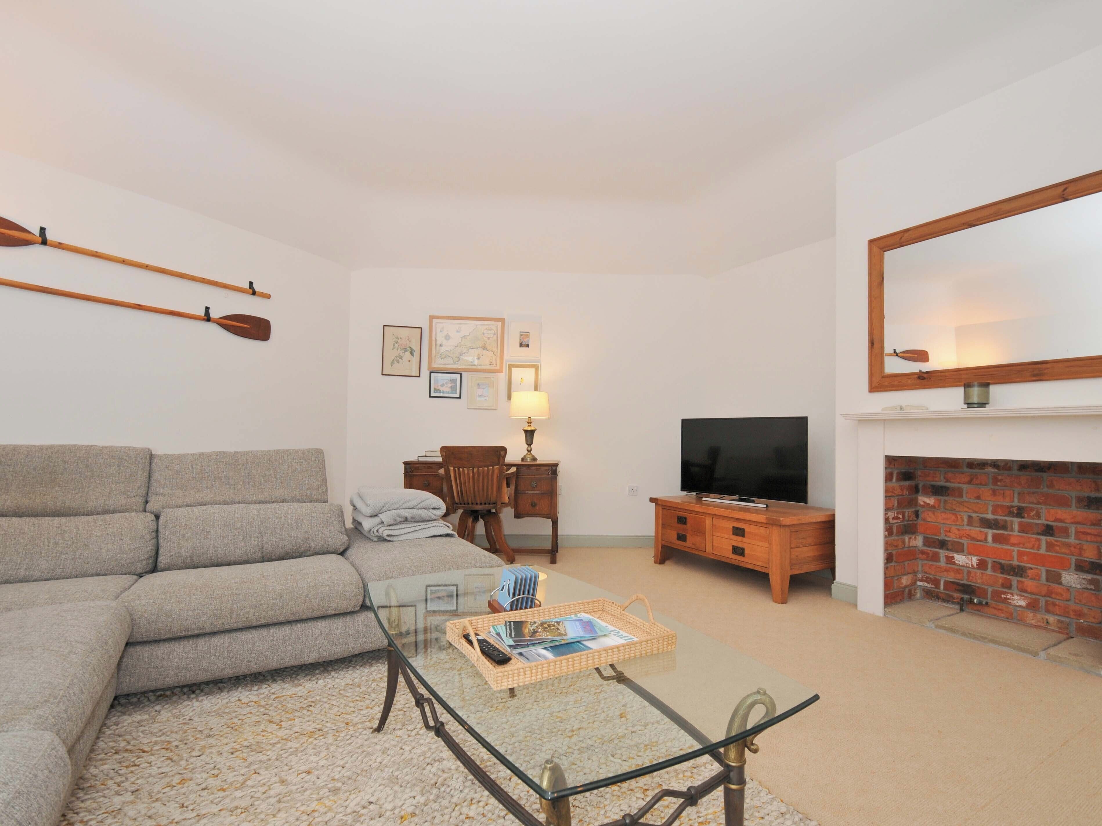 A living room with a sofa, a glass coffee table, a TV, a fireplace, and a desk with a lamp.