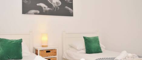 A hotel room with two beds, each with a green pillow and a patterned blanket. There is a wall-mounted picture of jellyfish above the beds.