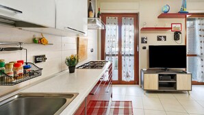 Une cuisine moderne équipée d’une cuisinière intégrée, d’un grand téléviseur et d’un coin repas agrémenté d’un tapis à carreaux rouges et blancs.