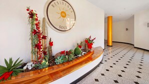 Un espace d’accueil avec un panneau circulaire portant l’inscription « RESIDENZA SOLE », un comptoir d’accueil en bois et un sol carrelé.