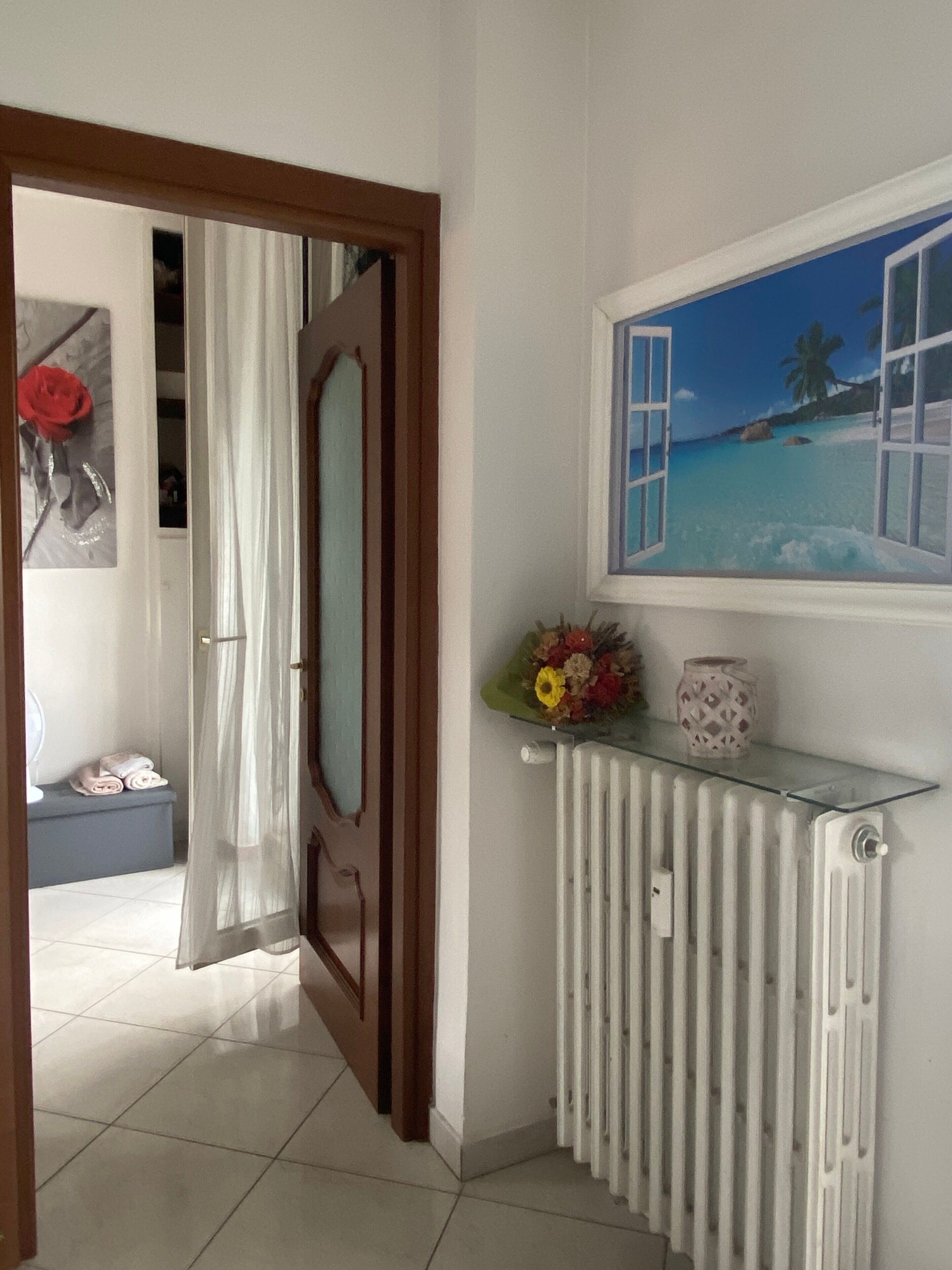 A hallway with a door leading to a room, a radiator, and a wall-mounted painting of a beach scene.