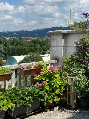 Jardí al terrat amb plantes i flors en testos, una estructura de pedra i vista del paisatge circumdant.