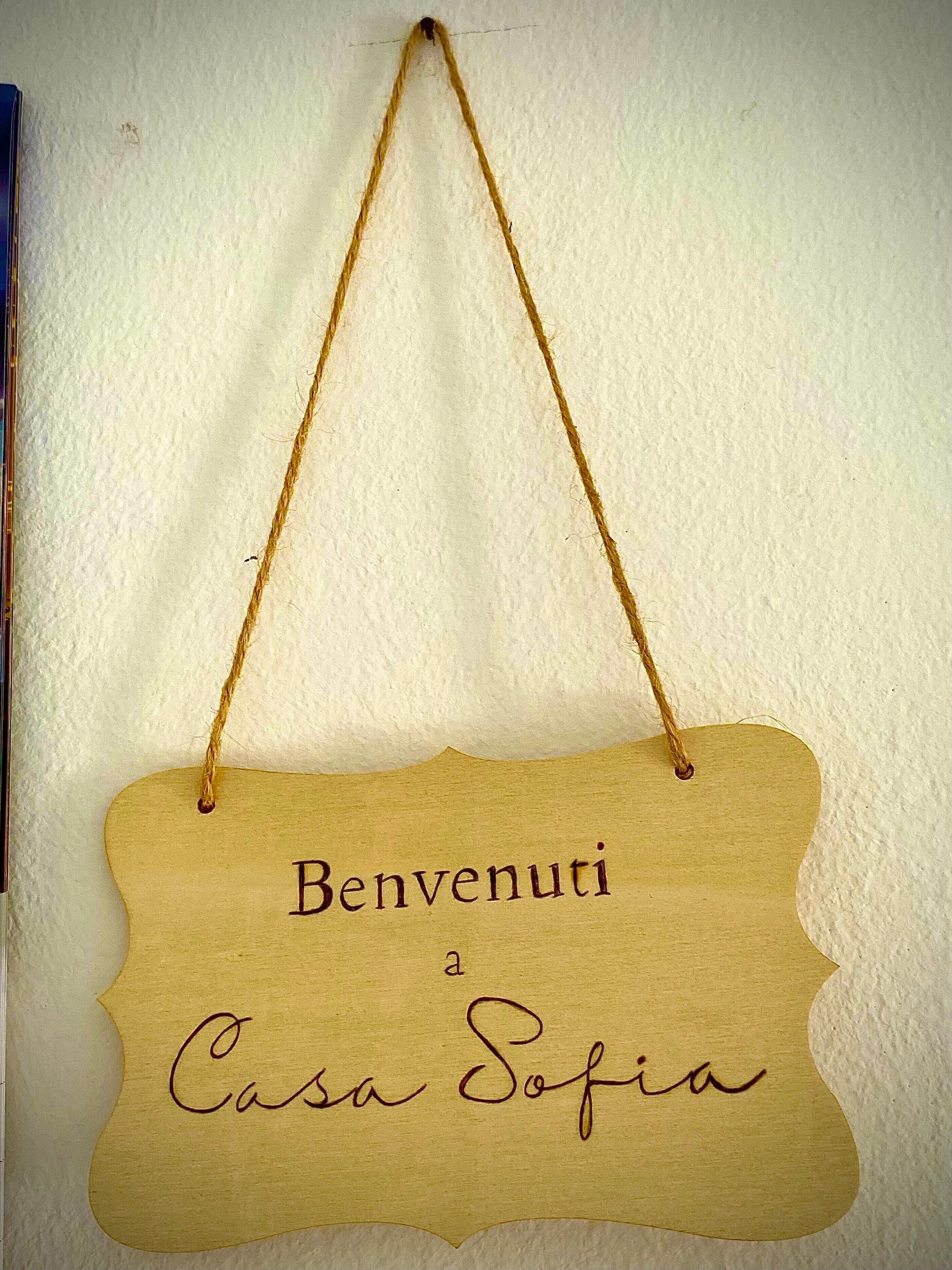 Ein hölzernes Schild mit der Aufschrift 'Benvenuti a Casa Sofia' an einer Wand.