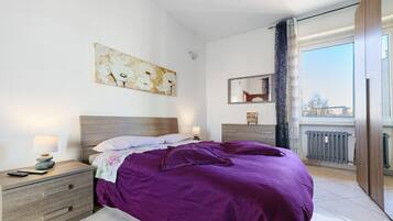 Une chambre à coucher avec un lit, une table de chevet, une lampe et une œuvre d’art accrochée au mur.