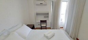 A hotel room with a bed, a desk, a chair, and a window with curtains. - COOND0102 - Ondina Residence (Salvador)