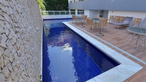 A swimming pool with a stone wall on one side and a patio area with outdoor furniture. - COOND0102 - Ondina Residence (Salvador)