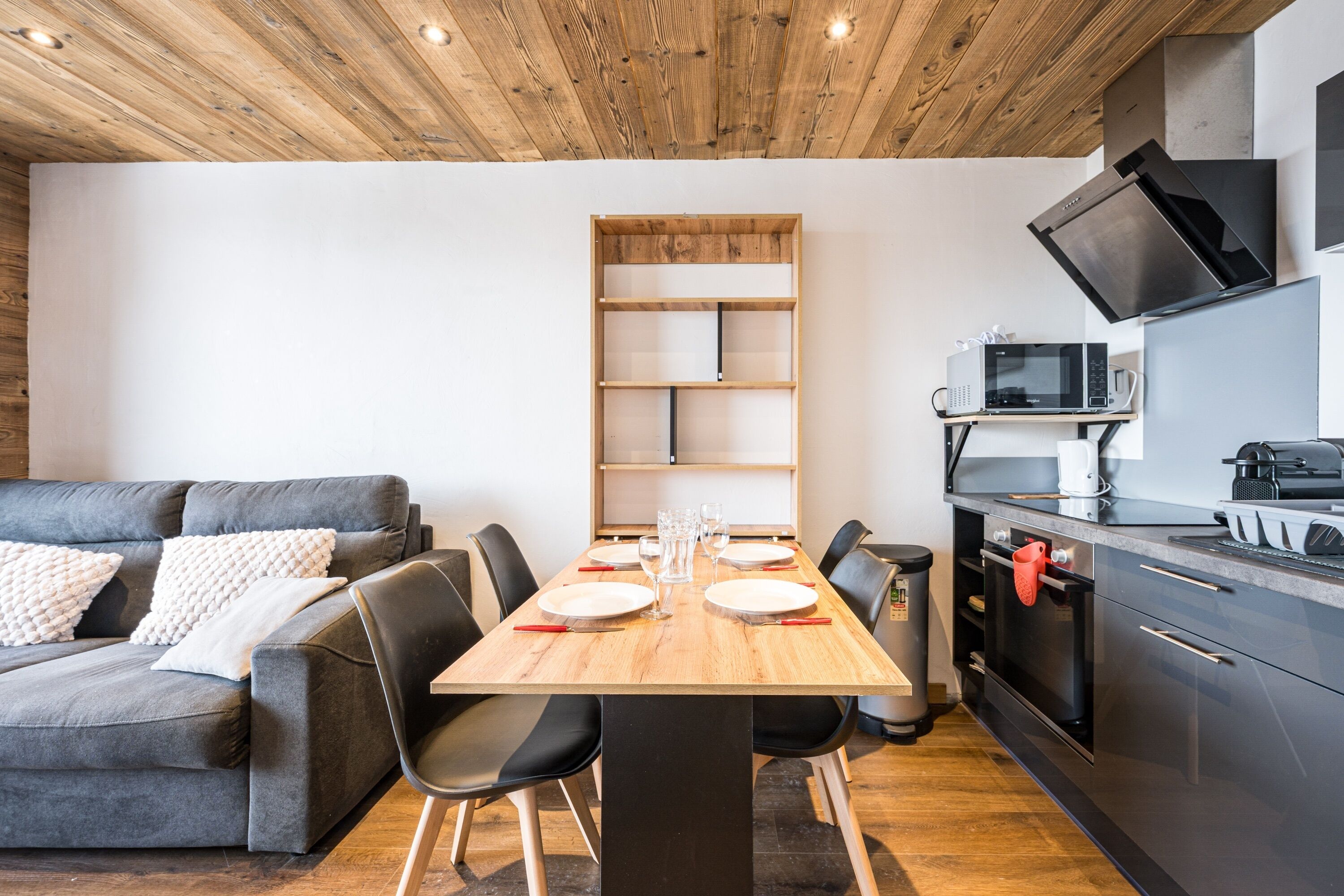 Una cocina moderna con una mesa de madera, sillas negras y un sofá gris.