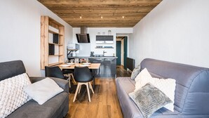 Een moderne woonkamer met een houten plafond, een eethoek met tafel en stoelen, en een keuken op de achtergrond.
