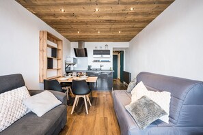 Ein modernes Wohnzimmer mit Holzbalkendecke, einem Essbereich mit Tisch und Stühlen sowie einer Küche im Hintergrund.