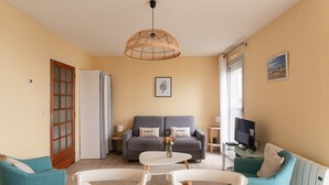 Ein modernes Wohnzimmer mit einer Couch, Sesseln, einem Esstisch, einem Fernseher und einer dekorativen Pendelleuchte.