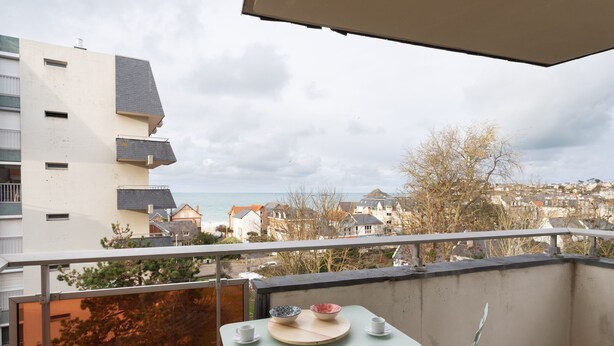 Ein Balkon mit Tisch und Stühlen mit Blick auf eine Stadtlandschaft und das Meer.