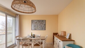 Ein Essbereich mit Tisch und Stühlen, einer Lampenschirm aus Weidwerk, einem gerahmten abstrakten Gemälde und Blick durch eine Schiebetür.