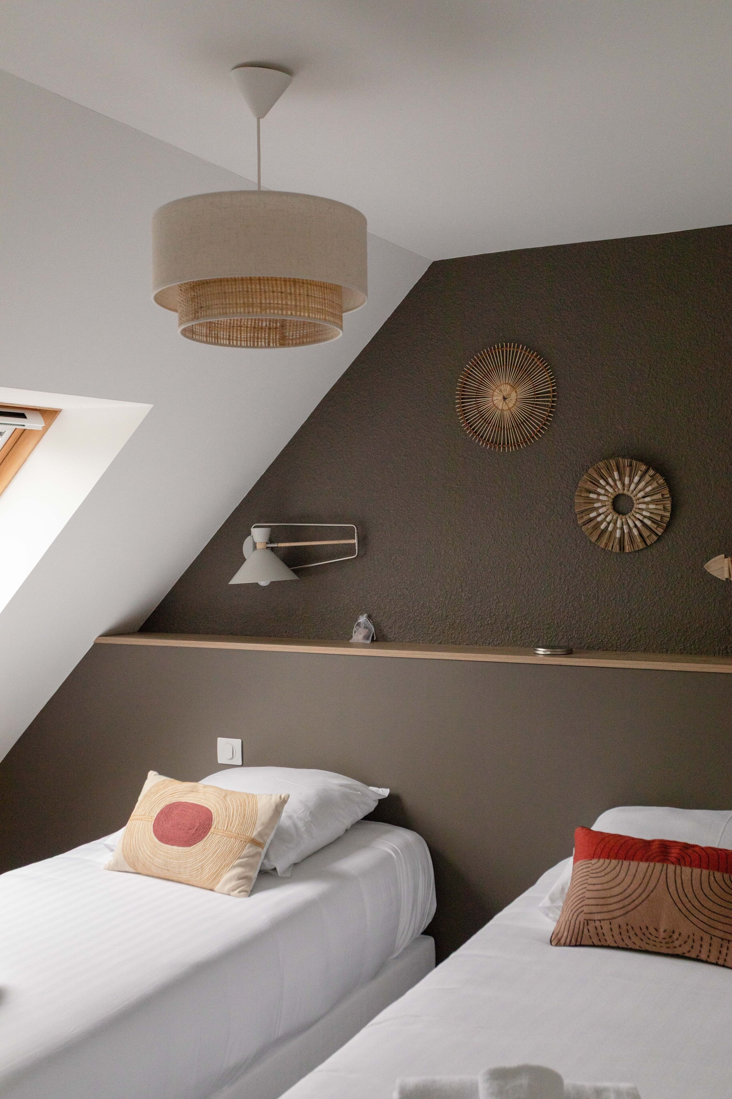 Una habitación de hotel moderna con dos camas, una lámpara de techo, decoración en la pared y una estantería con una lámpara.
