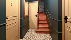 A narrow hallway with a wooden staircase, a door labeled '2', and patterned floor tiles. - Le 4 du Clos Fleuri - Proche Hippodrome (Caen)