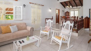 A spacious living area with a beige sofa, white rocking chairs, a white coffee table, and a dining table with chairs. - Soley Lodge - Climatisée avec terrasse et jardin (Plessis Nogent)